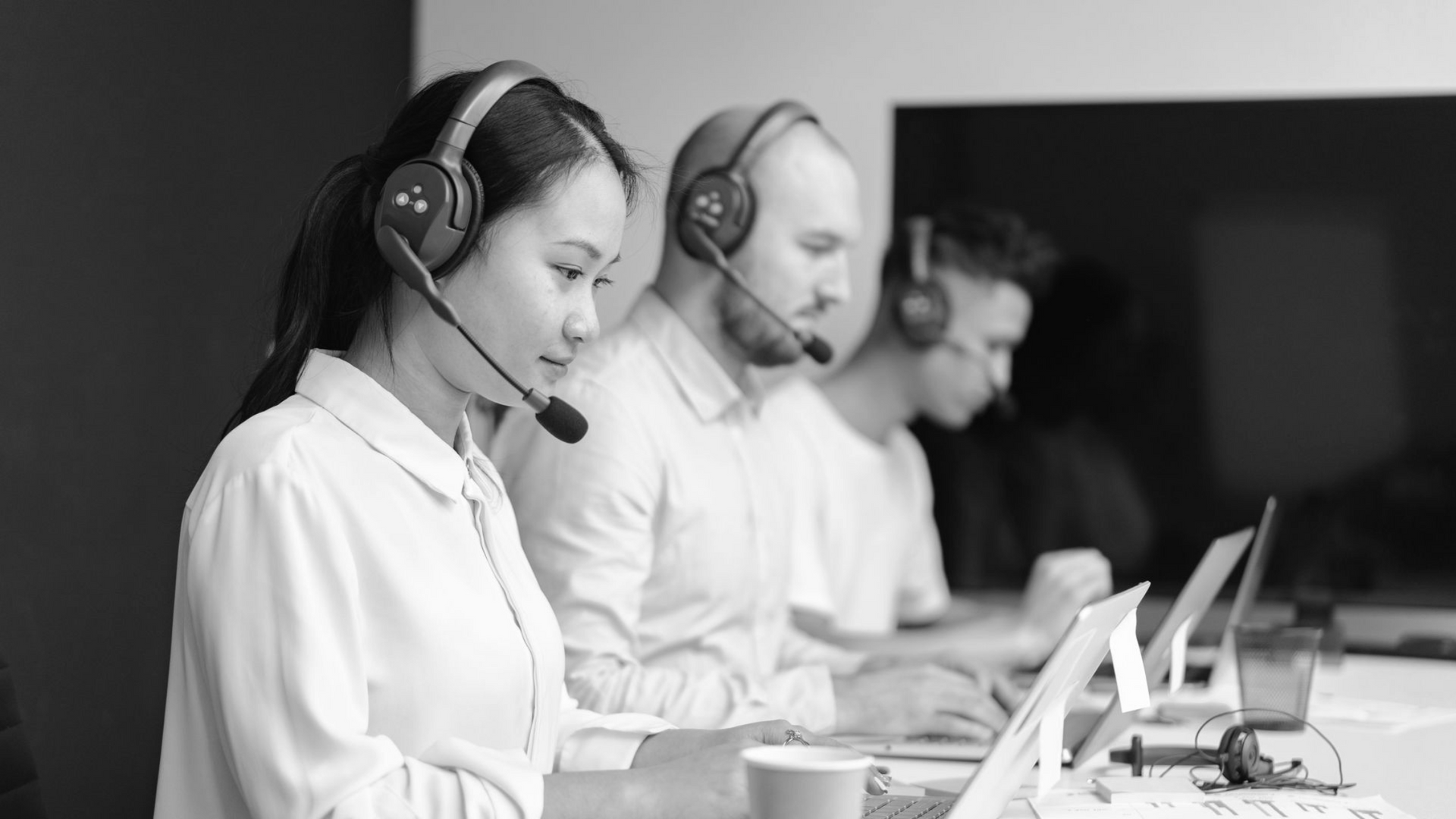 Customer support team wearing headsets working at laptops in a bright office.