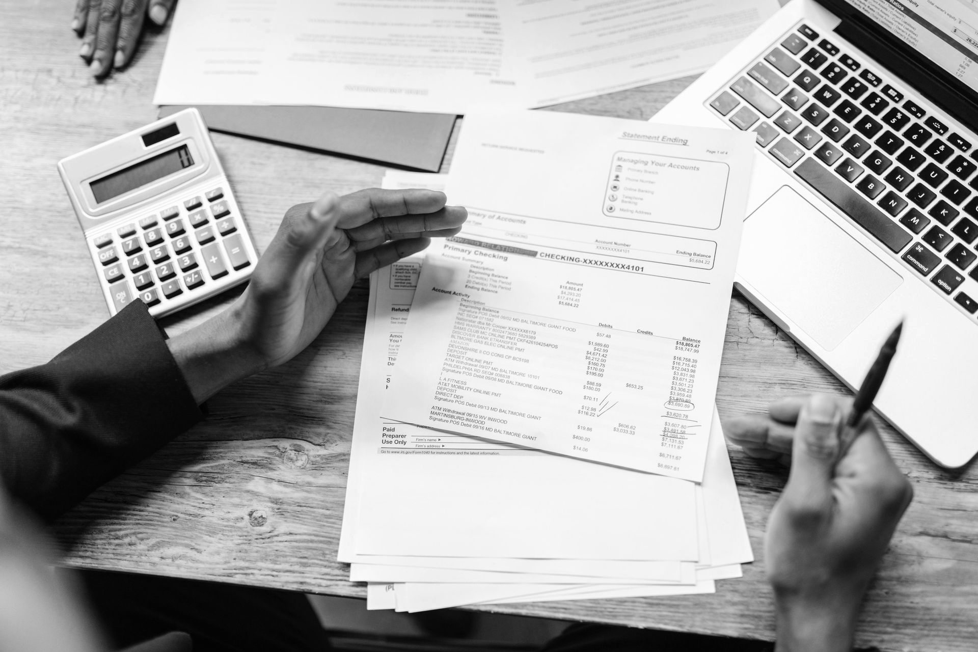 Hands reviewing paperwork beside a calculator and laptop on a desk