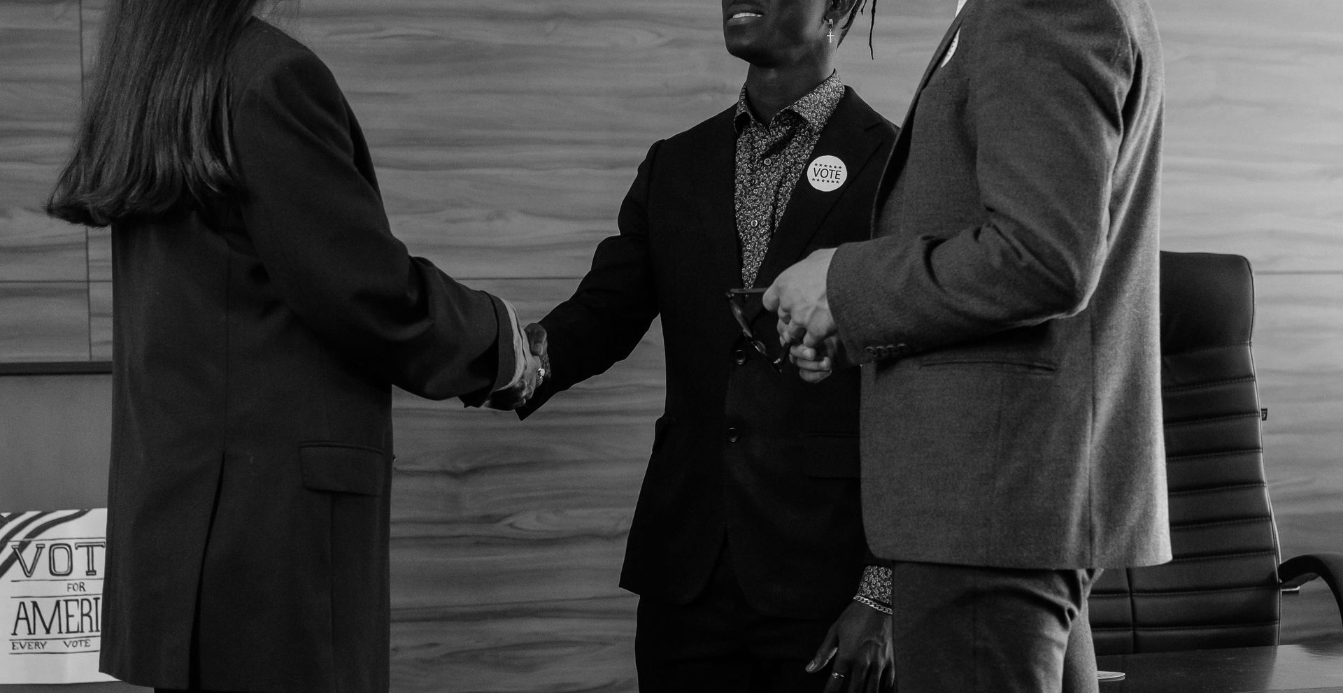 Three people in suits shaking hands in a formal indoor setting.