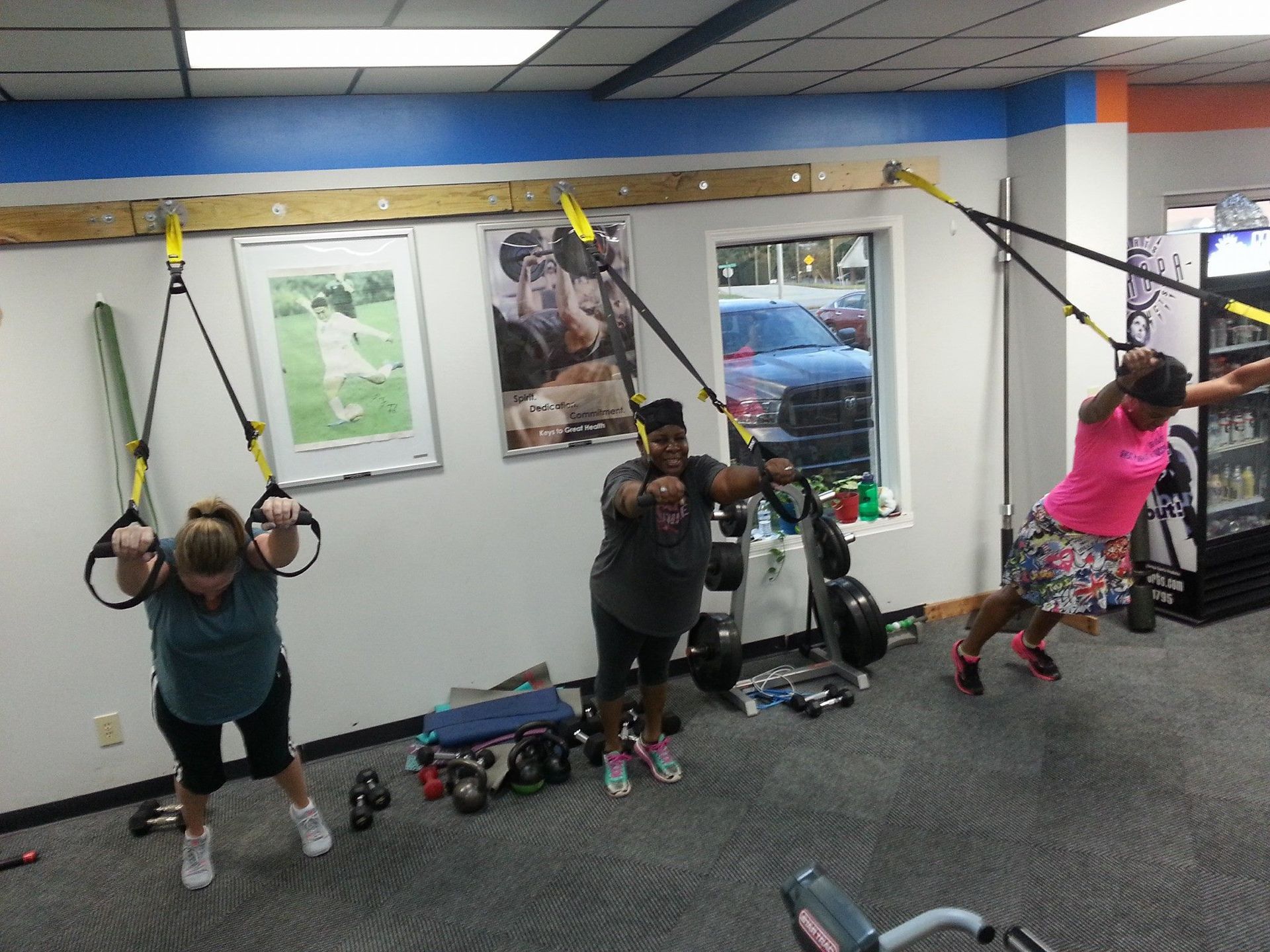 Three people exercising with suspension trainers in a gym.