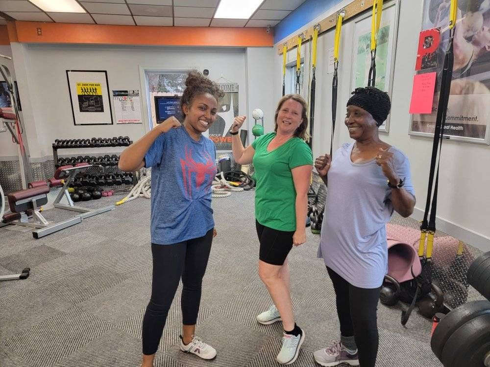 Three women in a gym, smiling and flexing their biceps.