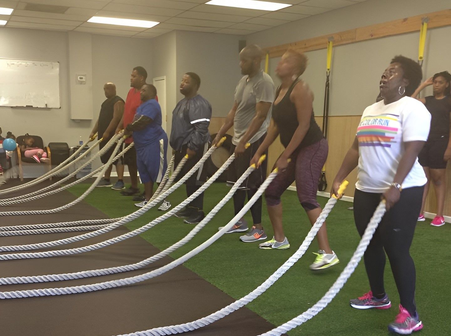 Group exercising with battle ropes in a gym; people are waving the ropes; artificial turf floor.