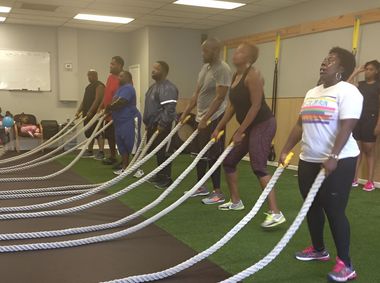 Group exercising with battle ropes in a gym; people are waving the ropes; artificial turf floor.