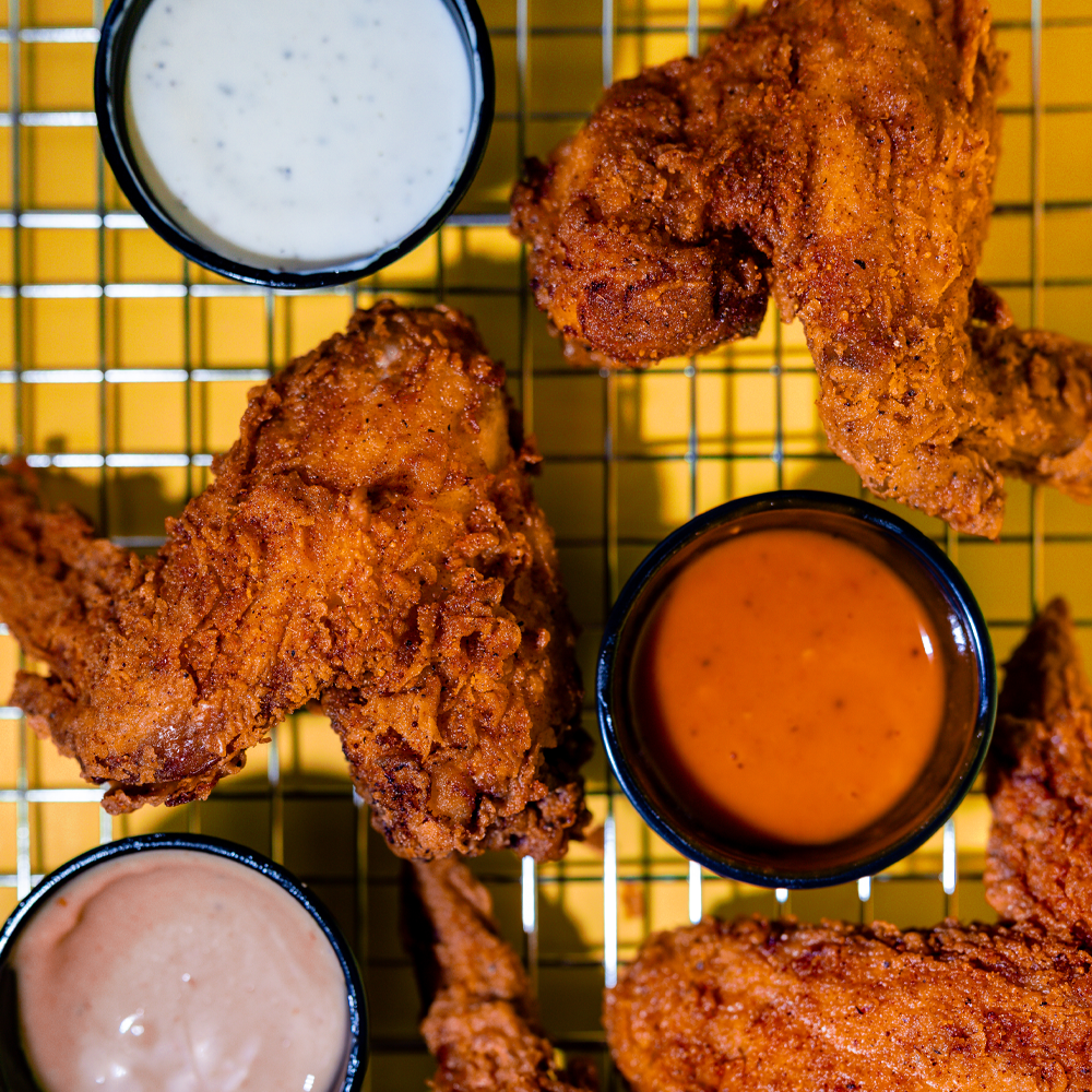 Whole chicken wings on a cooling rack with cup of sauce placed around.