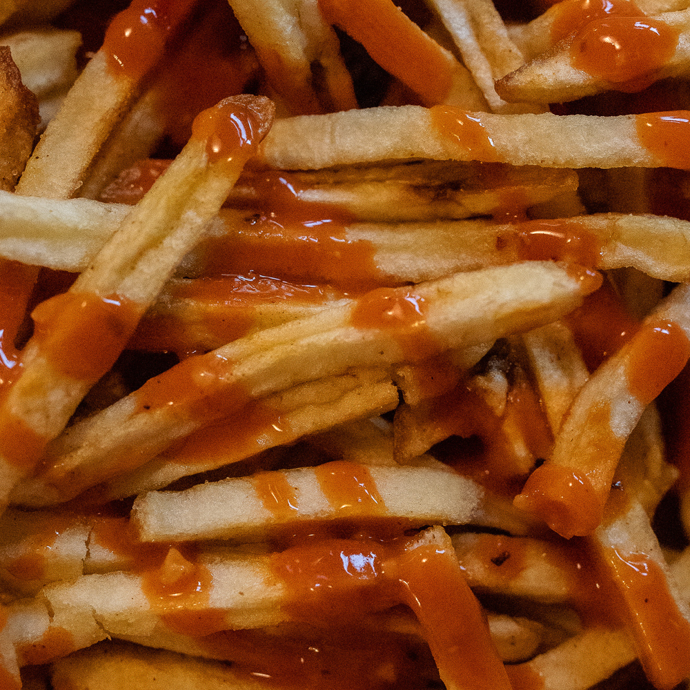 Close up of fries with hot sauce drizzled on top.