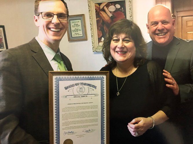 A man is sitting on a couch talking to a woman who is holding a clipboard.