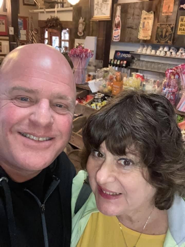A man is sitting on a couch talking to a woman who is holding a clipboard.