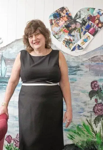 A woman in a black dress is standing in front of a painting of a heart.