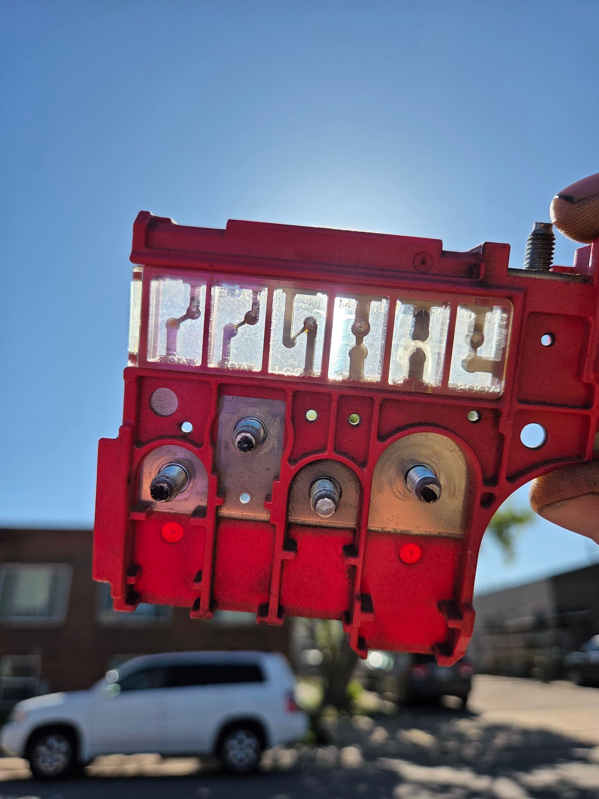 Red and clear car part held up to the sun; visible lettering and metallic components; blurry outdoor background | Freebird Automotive