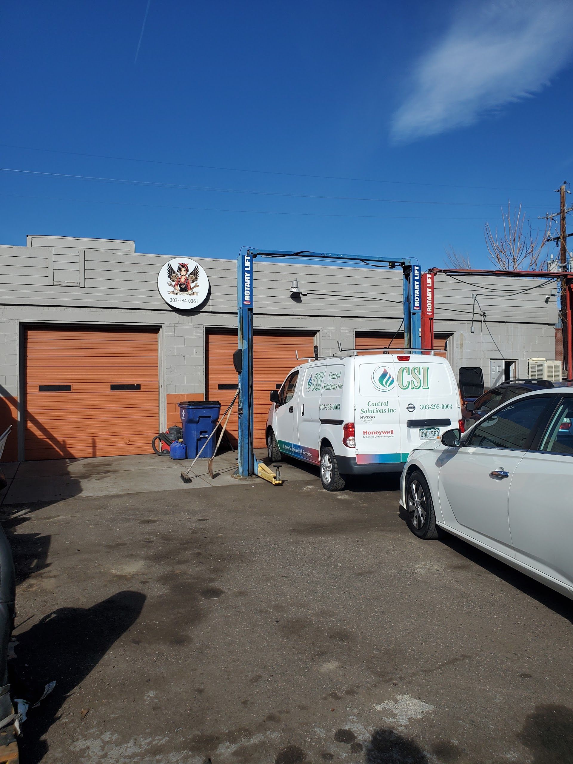 Exterior of auto shop with orange doors, a service van, car lift, and blue sky | Freebird Automotive