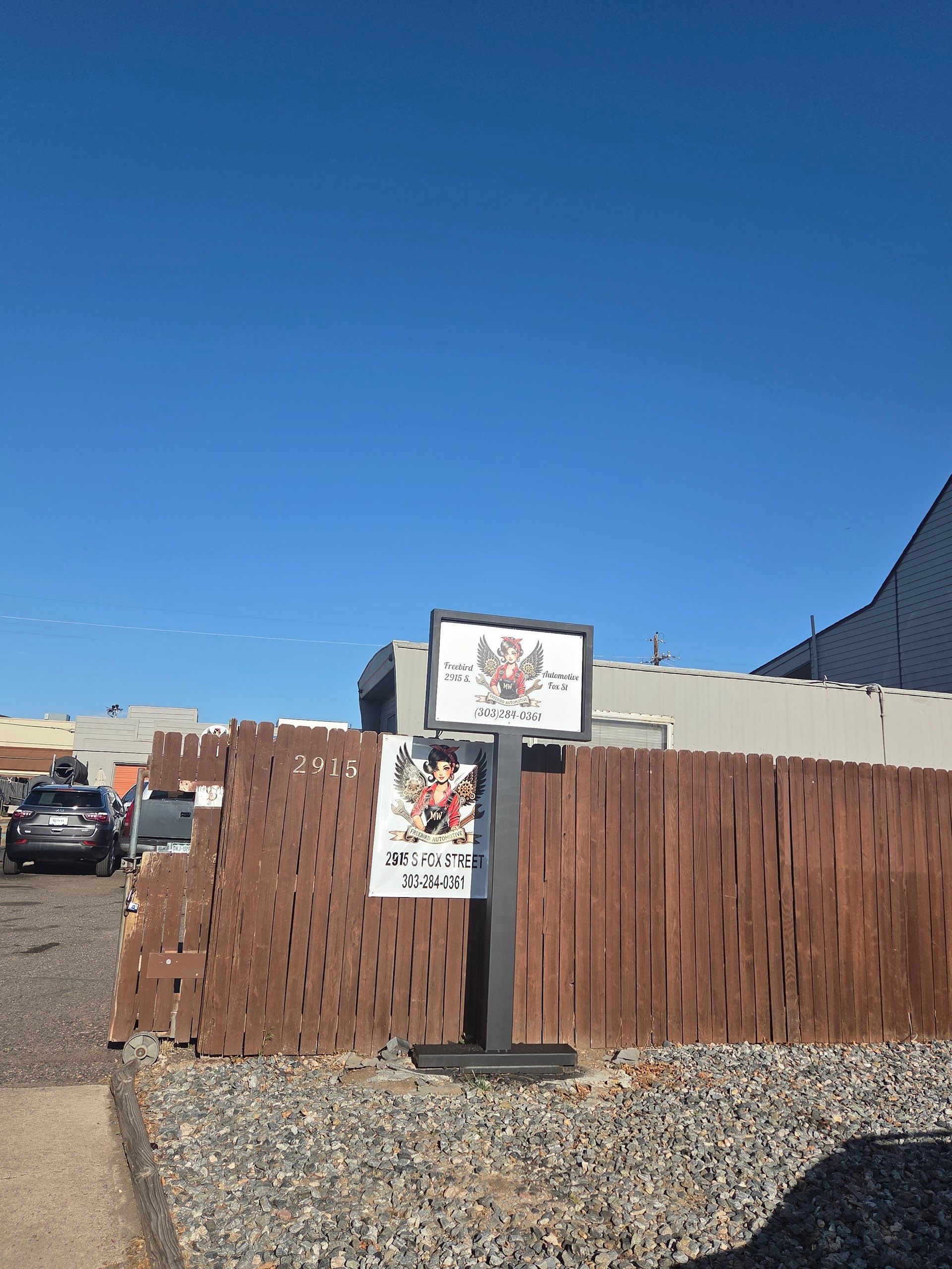 A street-level view of a business sign and fence | Freebird Automotive