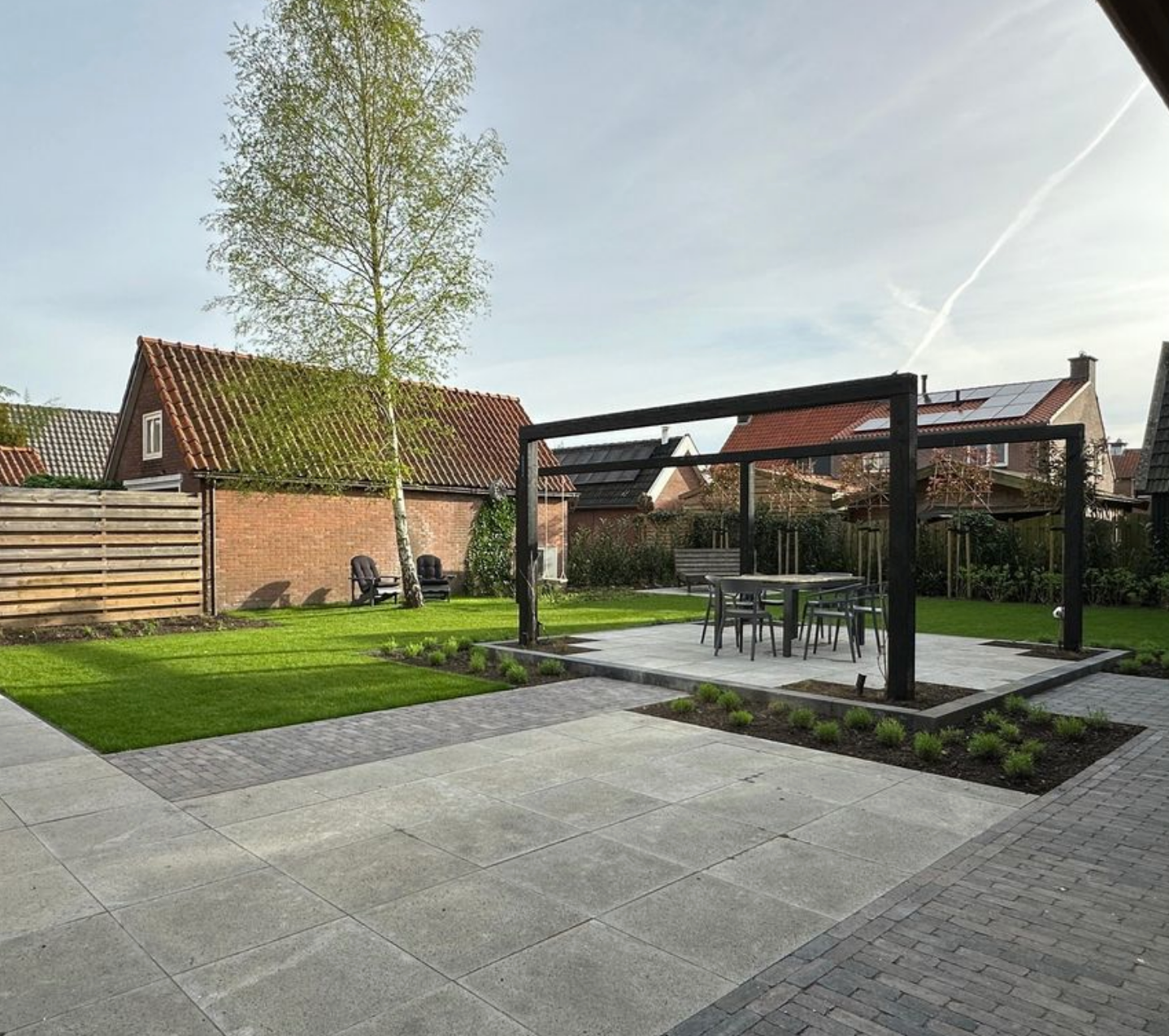 Een achtertuin met een tafel en stoelen onder een pergola.