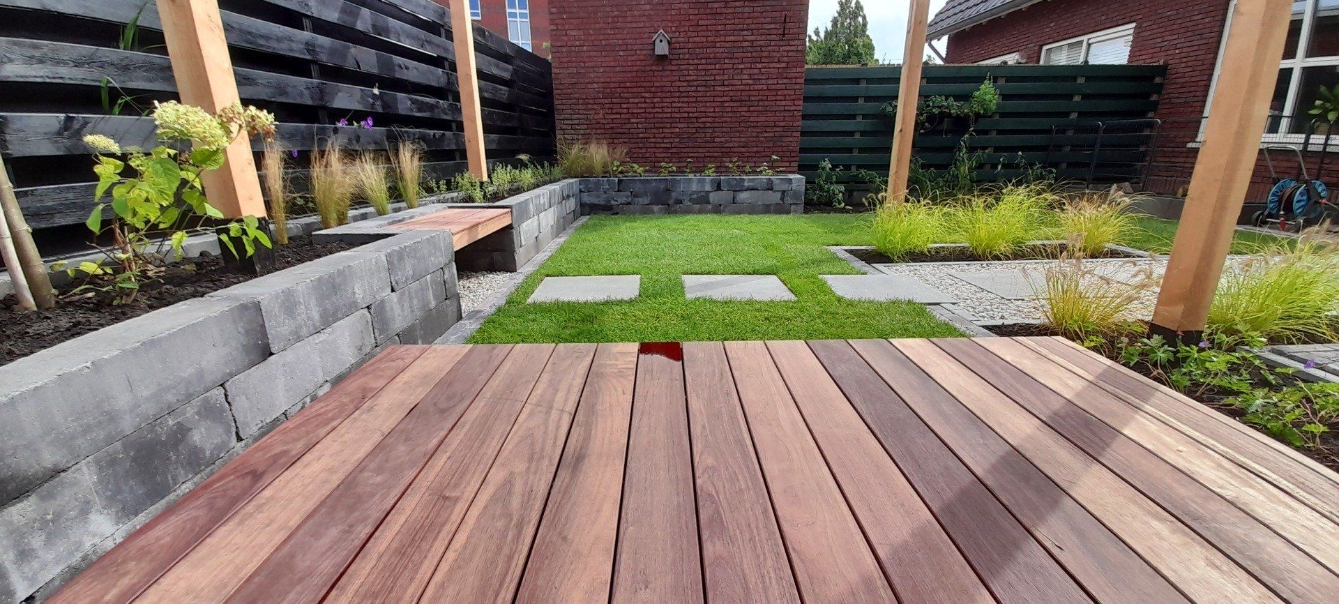 Er is een houten terras in het midden van een tuin.