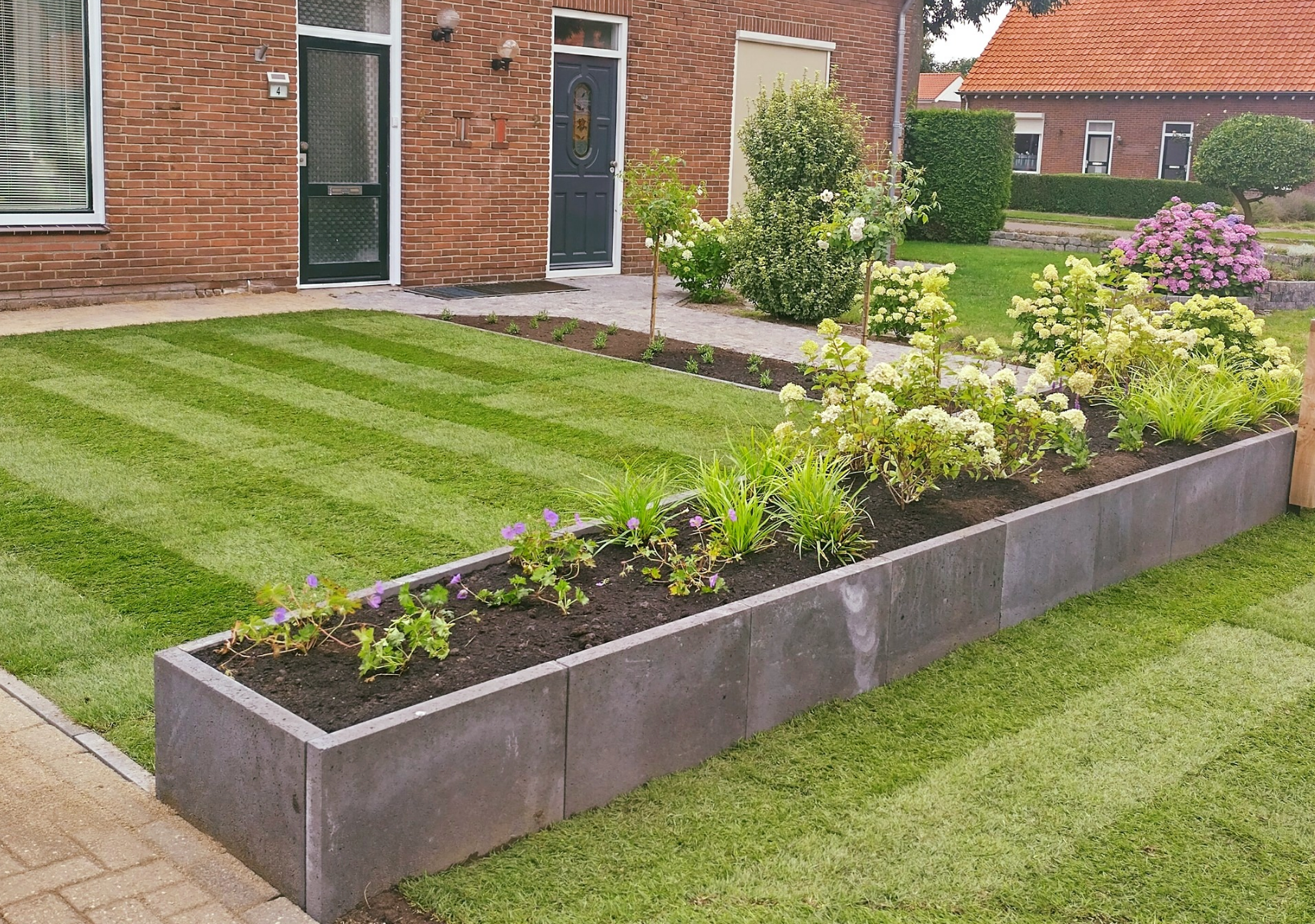 Een strak groen gazon met plantenbakken ervoor gevuld met diverse planten.