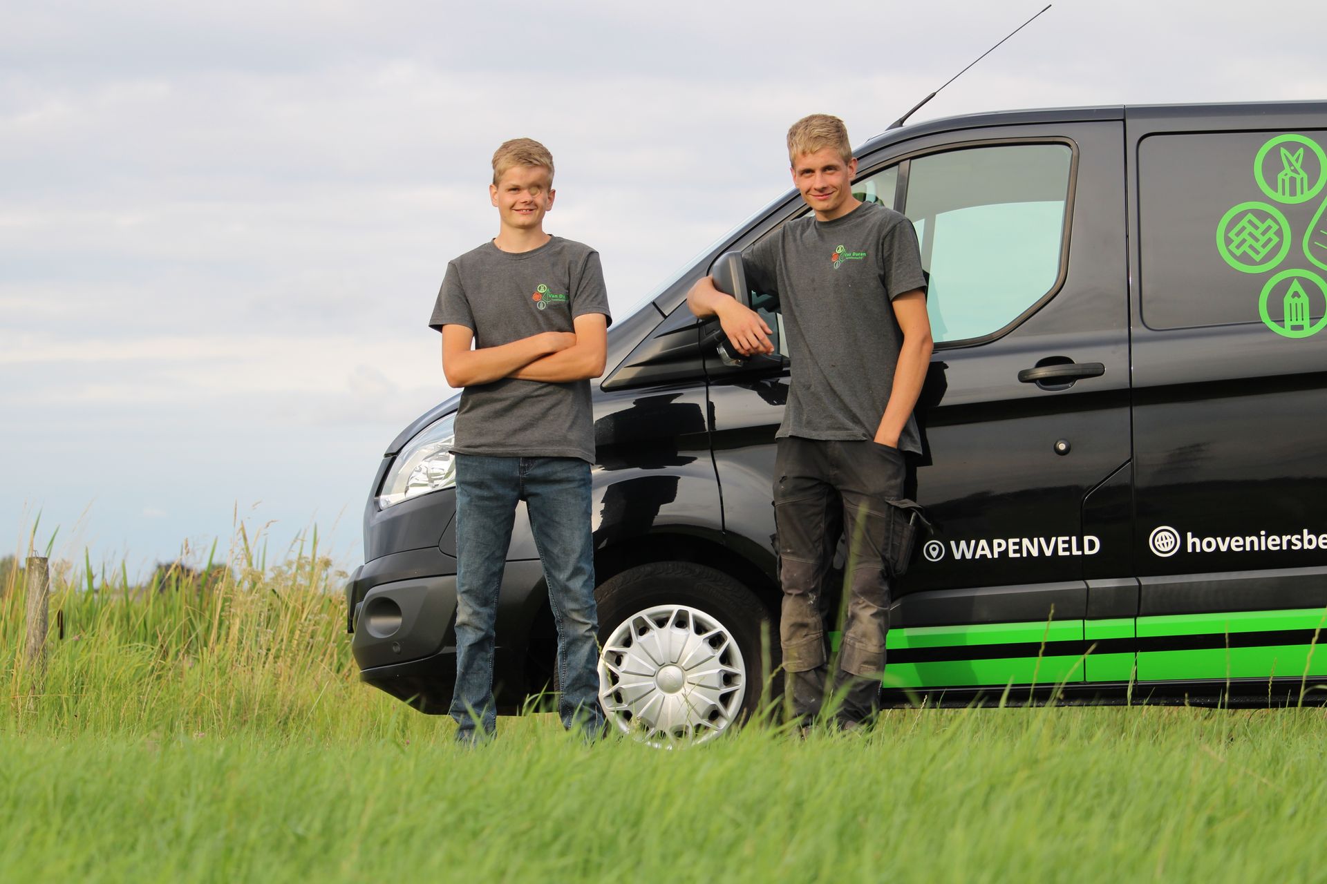 Hoveniers Niels en Maarten van Duren staan ​​naast hun zwarte werkbus. 