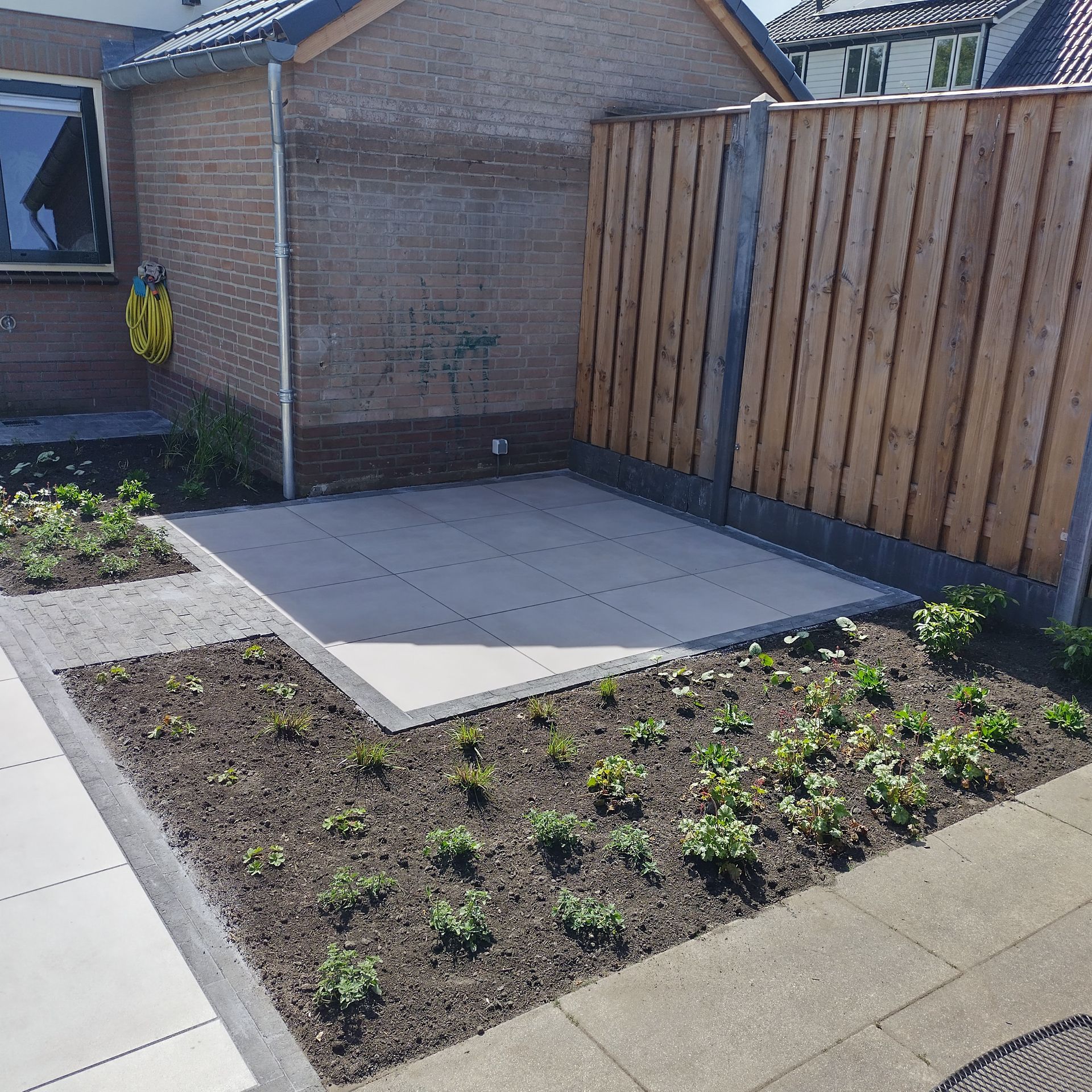 Een tuin met een terras van keramische tegels omringt door planten.