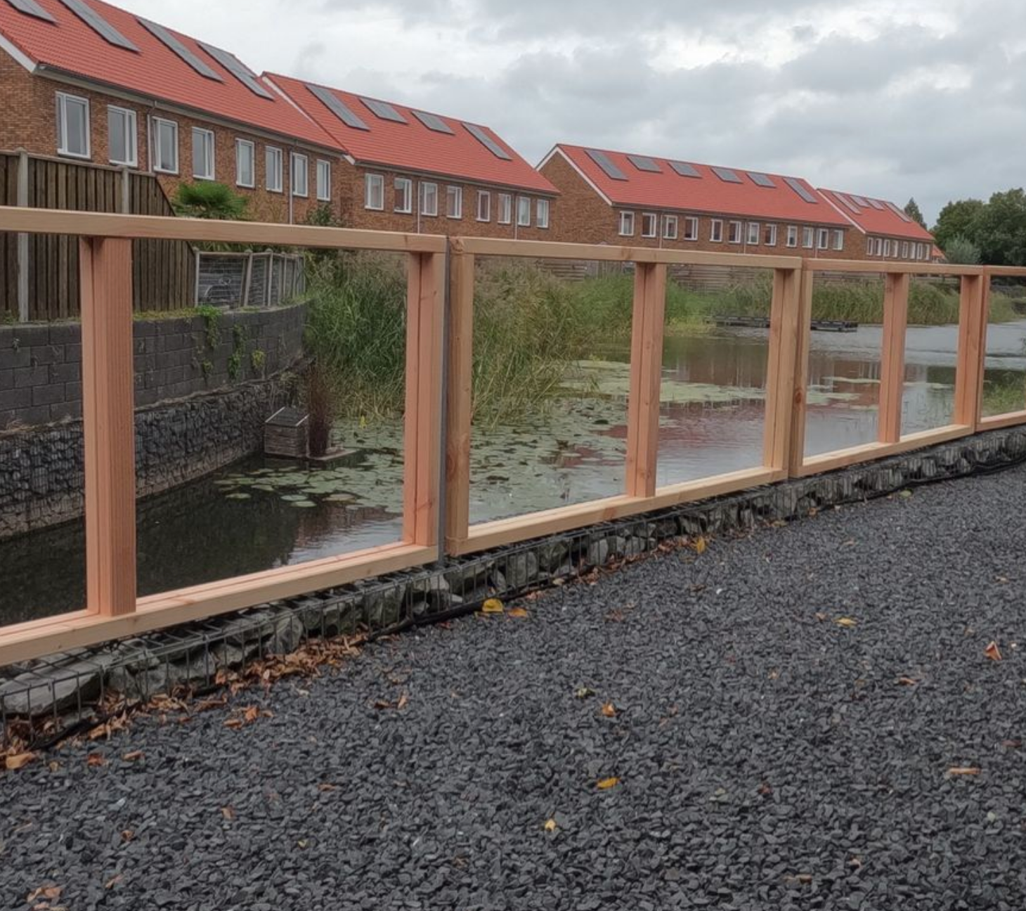 Een transparante schutting omringt door een waterpartij met huizen op de achtergrond.