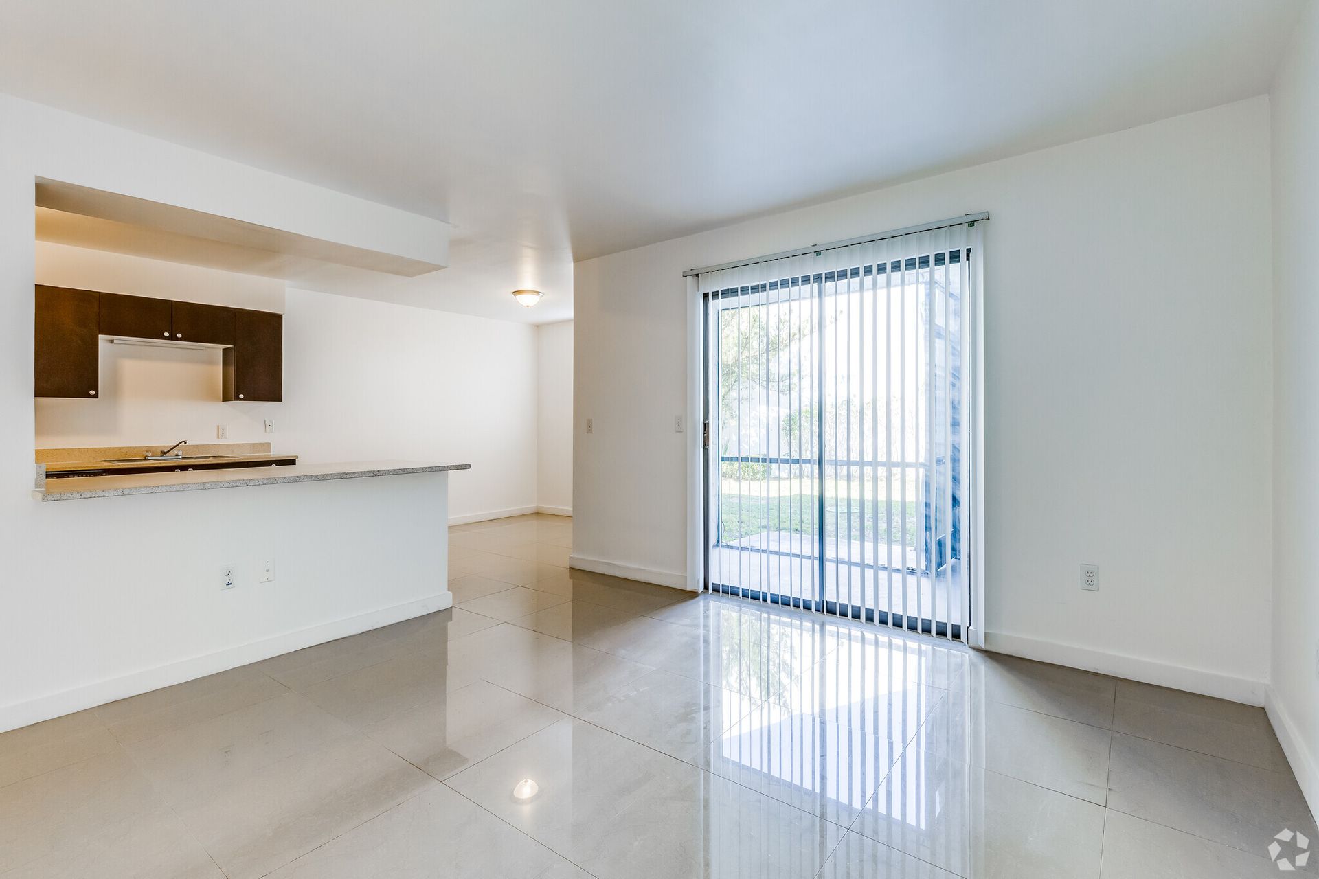 An empty living room with a sliding glass door and a kitchen.