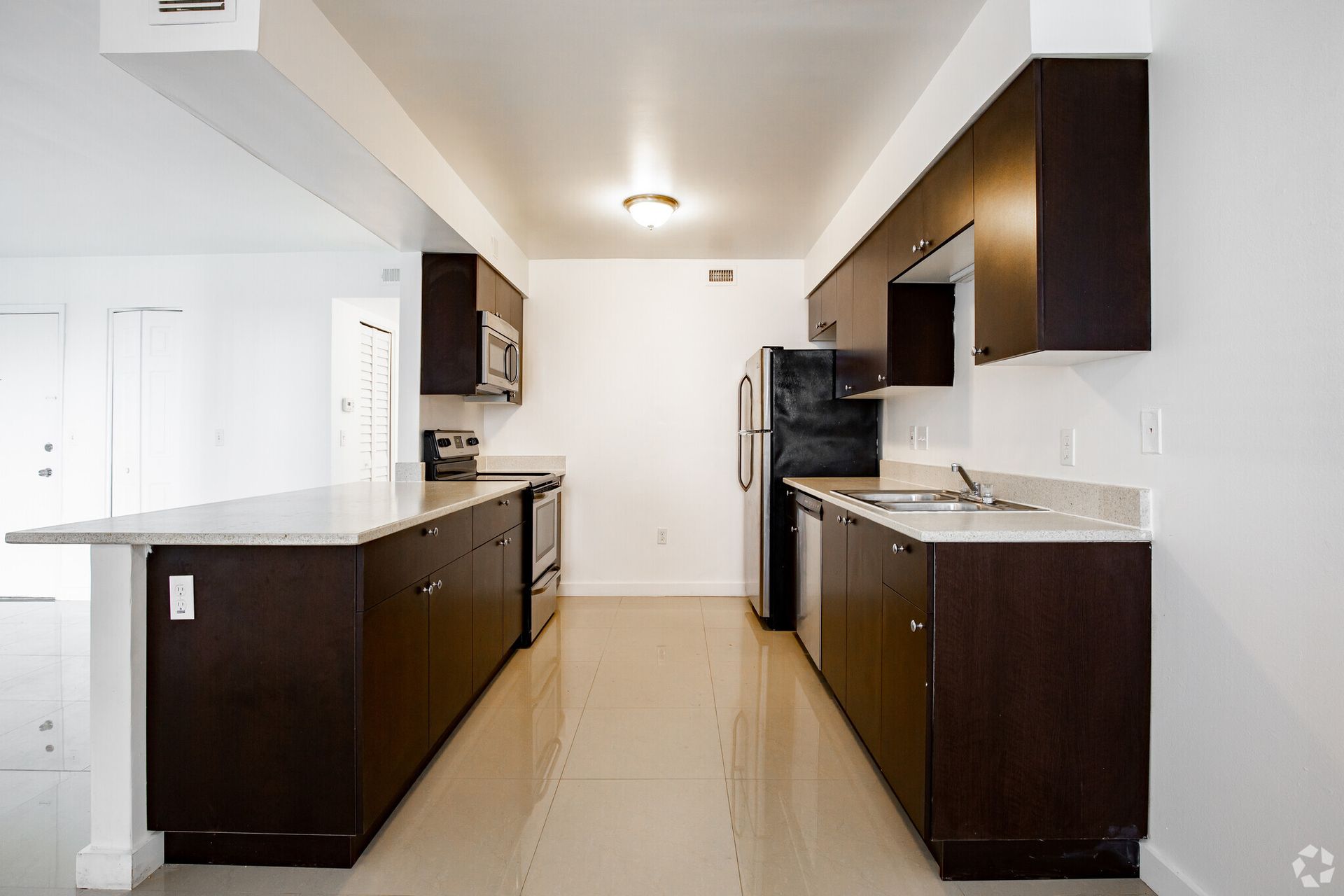 An empty kitchen with brown cabinets and stainless steel appliances