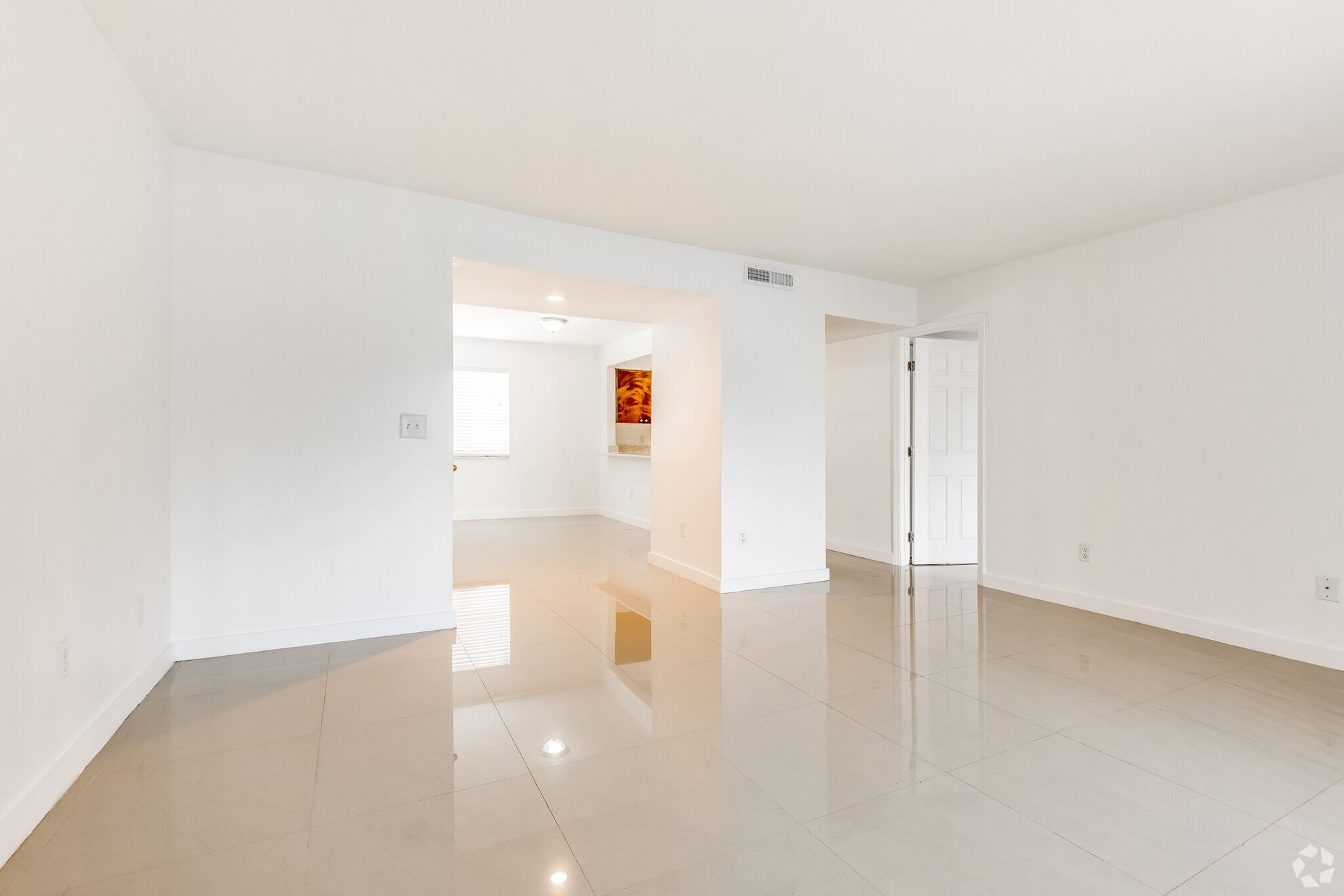 An empty living room with white walls and a tiled floor.