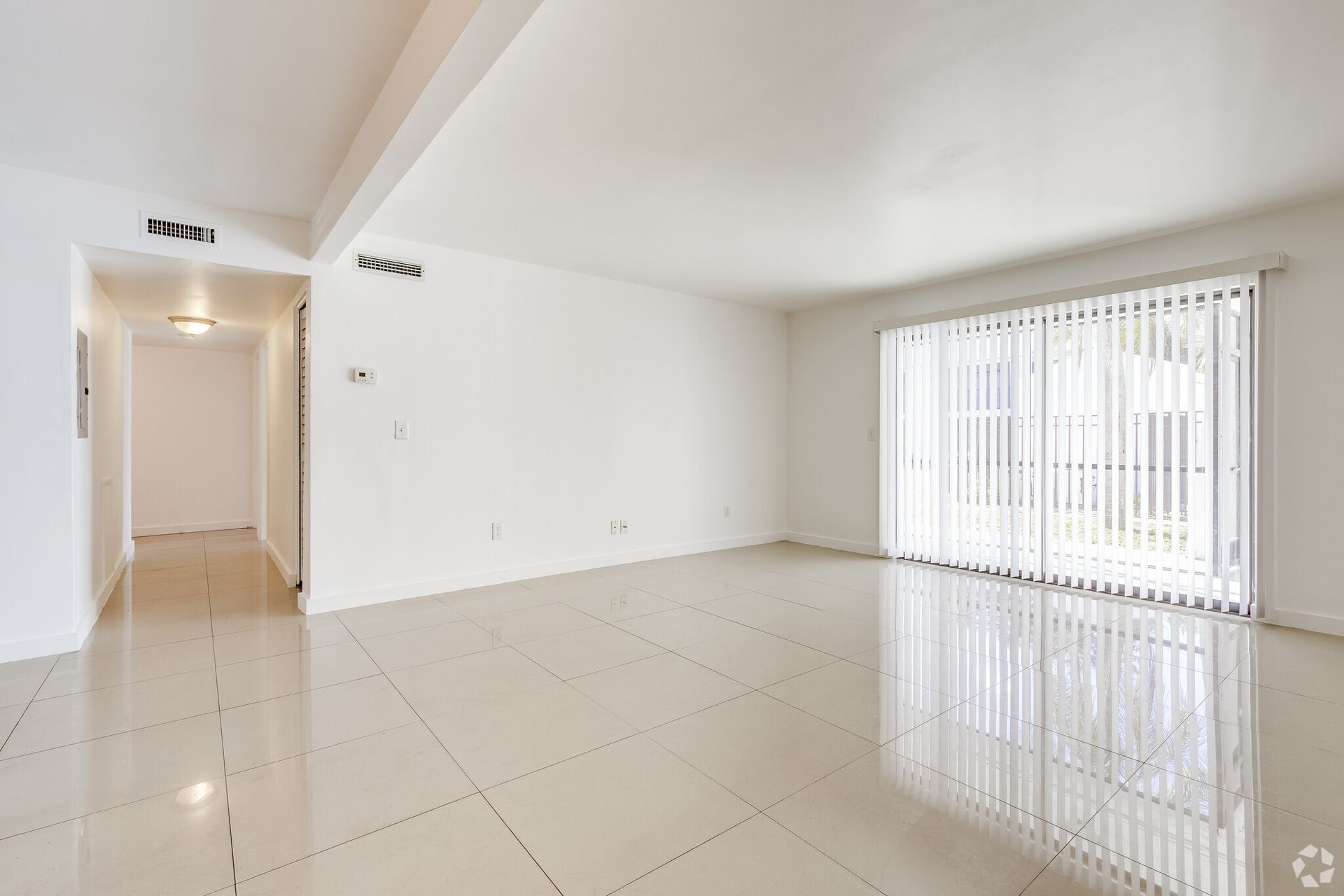 An empty living room with sliding glass doors and blinds.