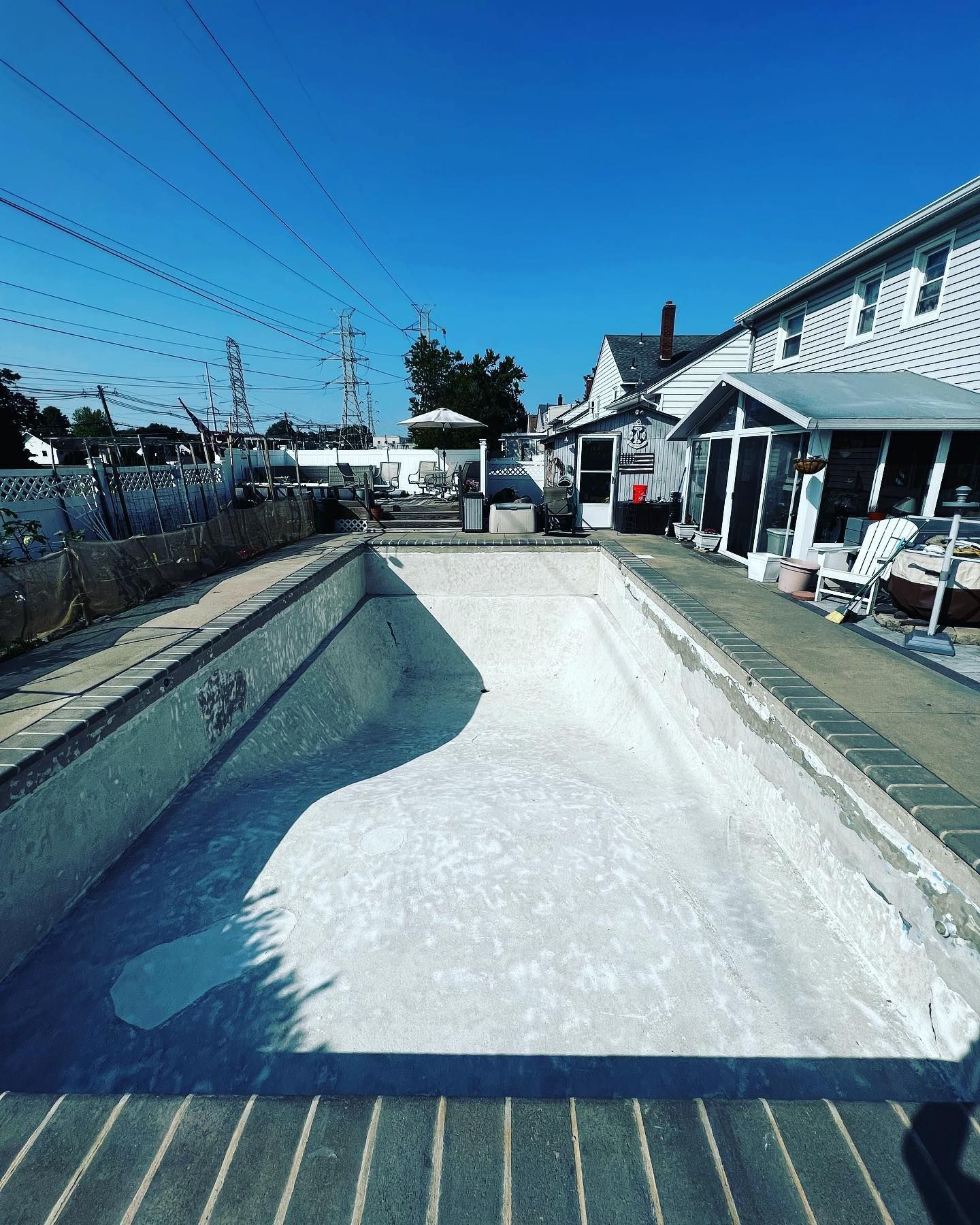 An empty swimming pool in a backyard with a house in the background.