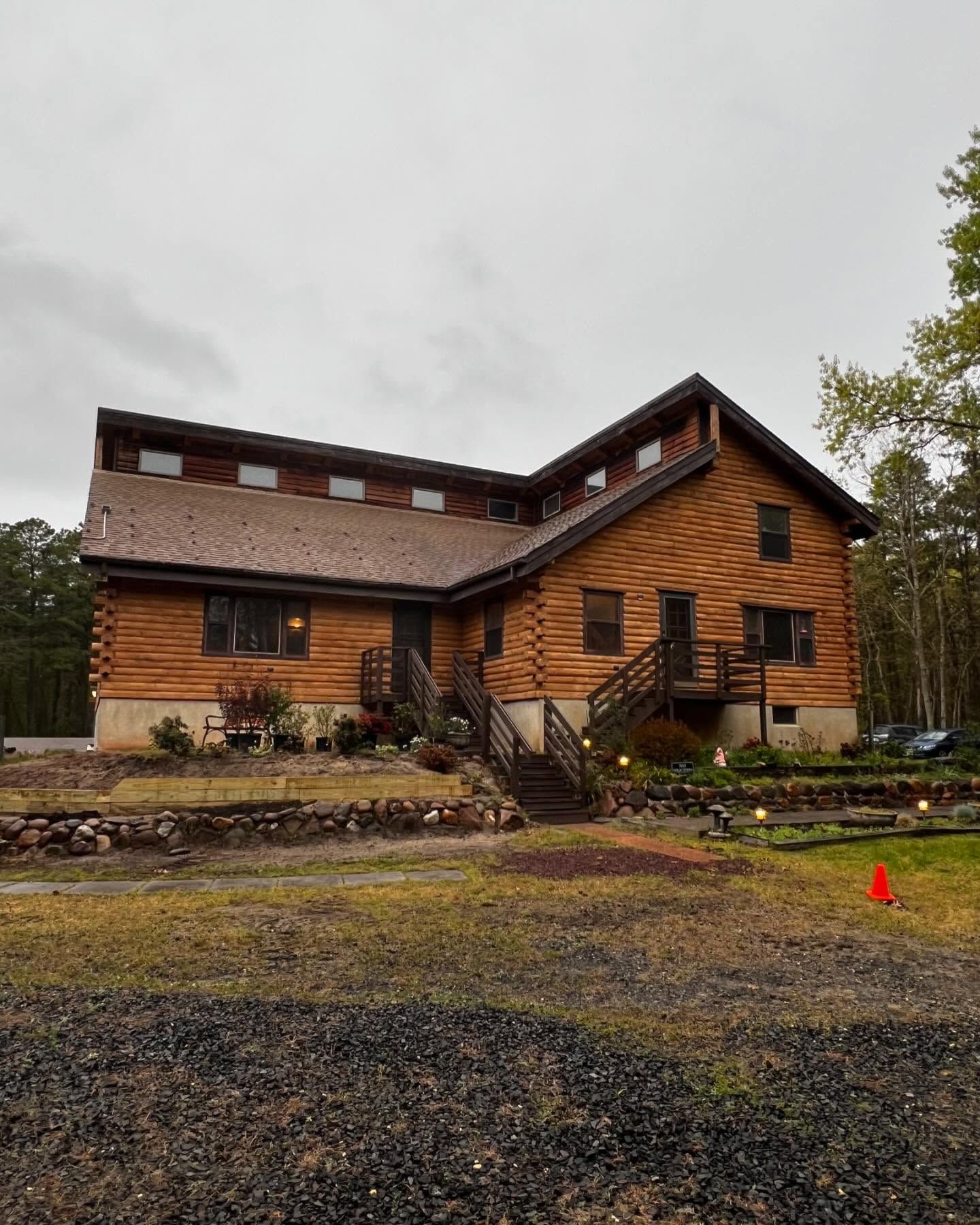 A large wooden house with stairs leading up to it is surrounded by trees.