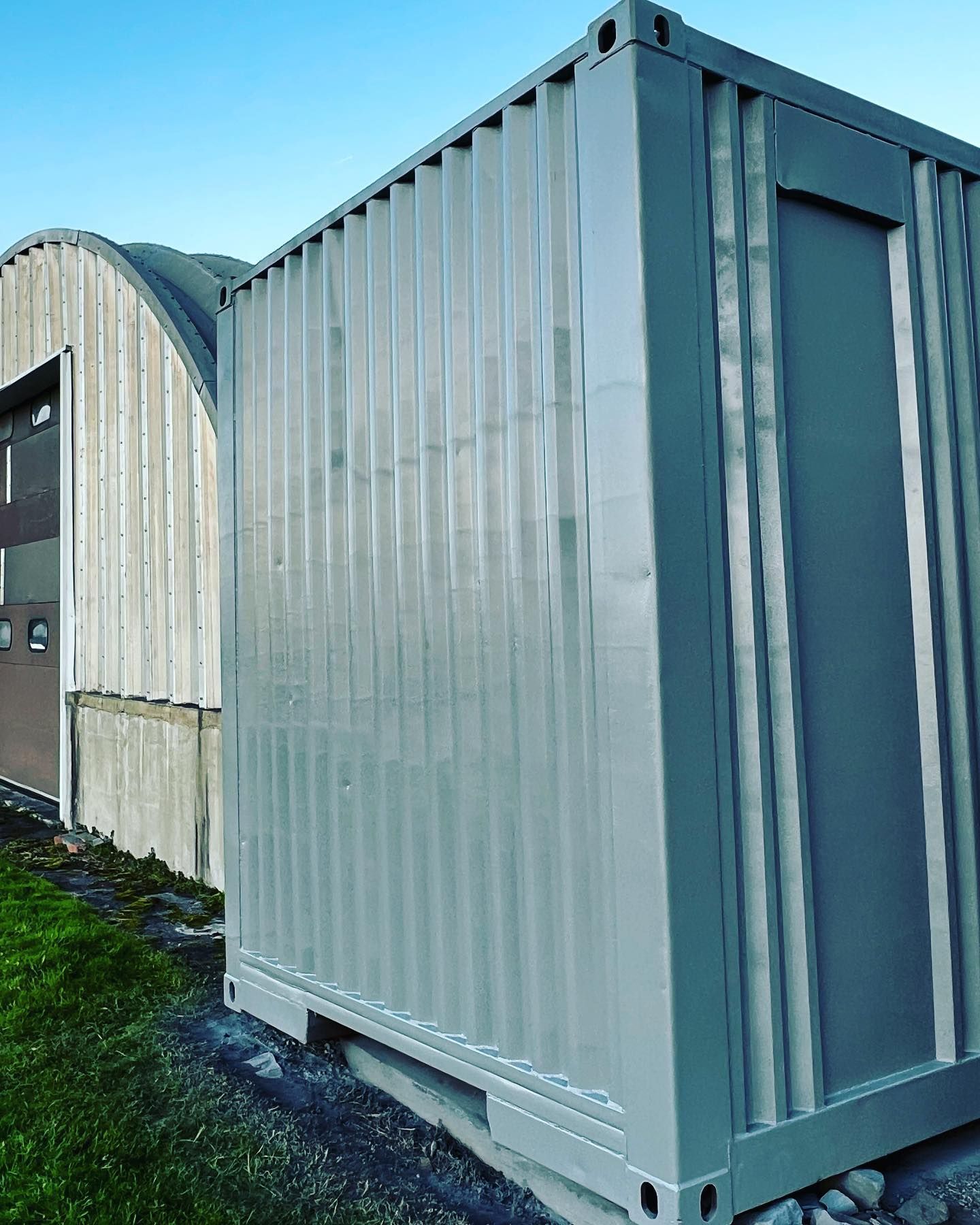 A gray shipping container is parked in front of a building.