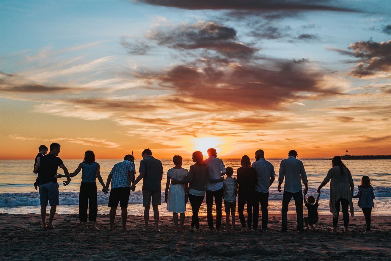 Um grande grupo de pessoas está na praia de mãos dadas ao pôr do sol.