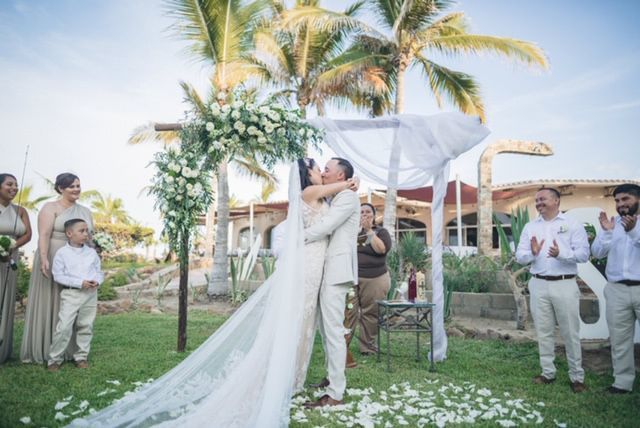 Una novia y un novio se besan bajo un dosel en la ceremonia de su boda.