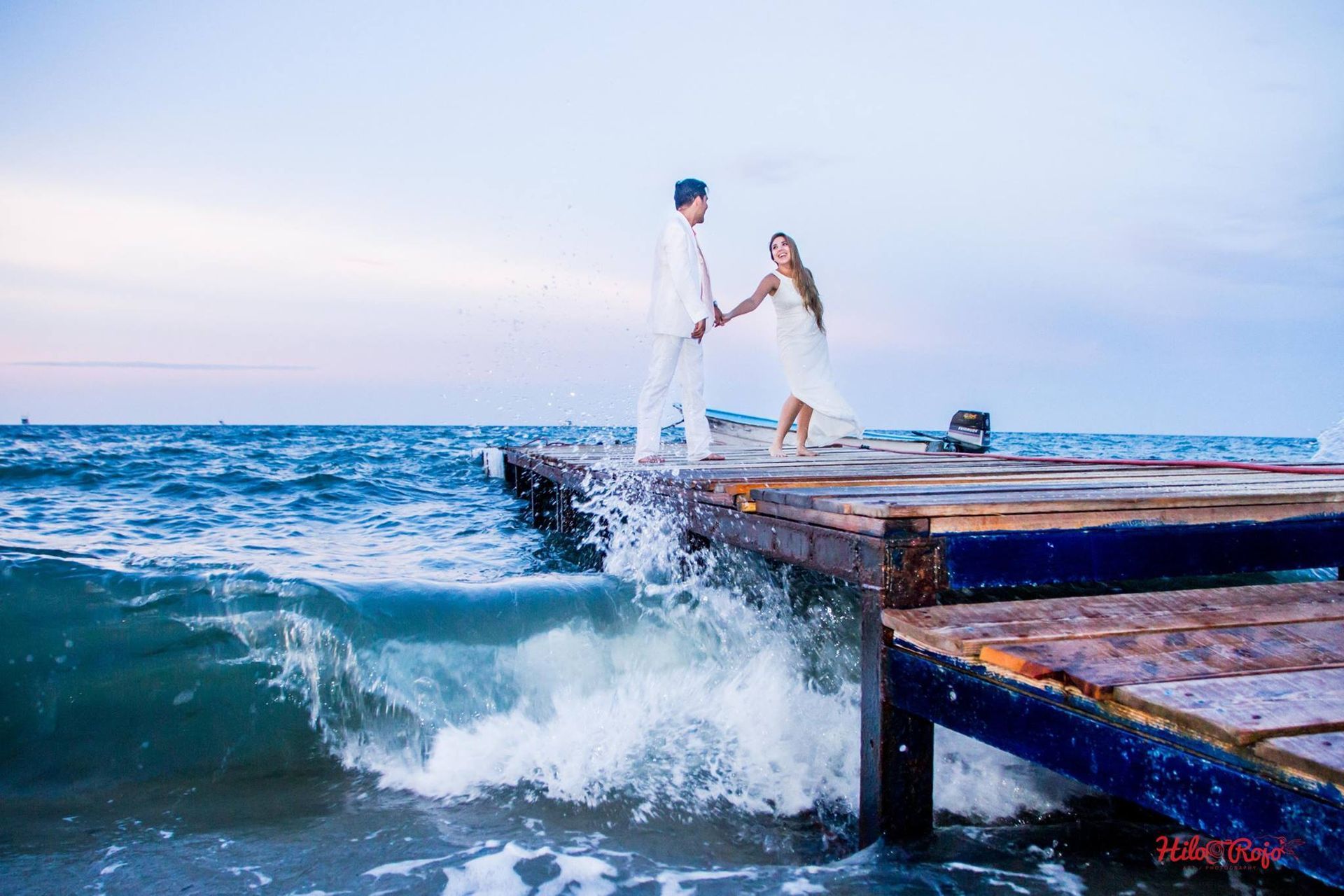 Un hombre y una mujer están parados en un muelle en el océano tomados de la mano.