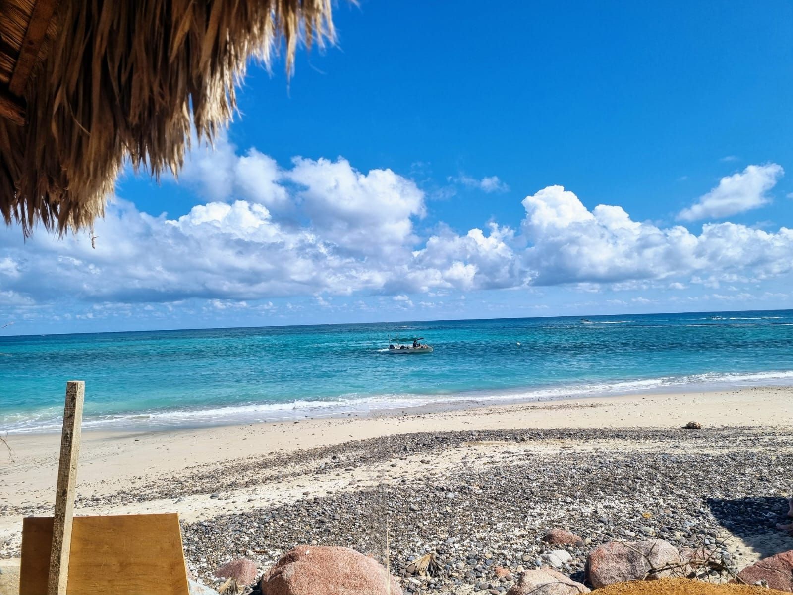 Una playa con un barco en el agua y un techo de paja.