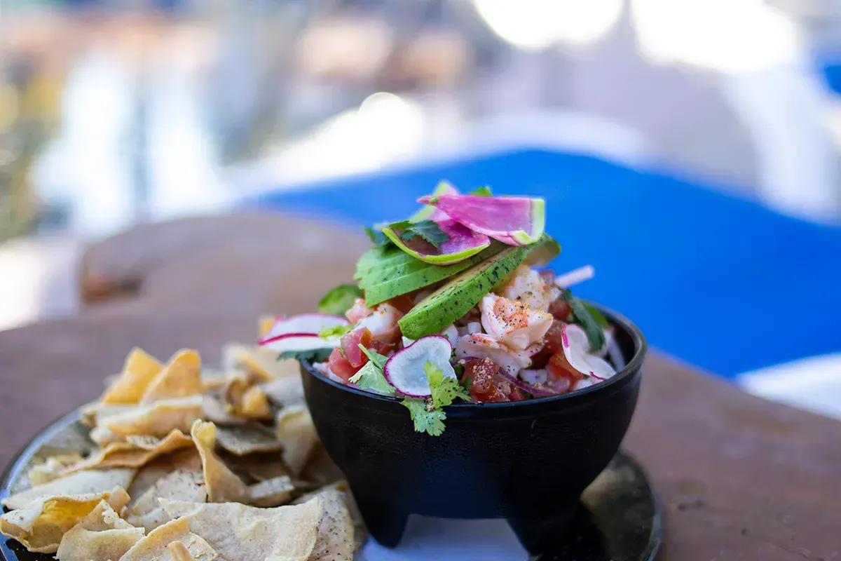 Uma tigela de comida com abacate e camarão ao lado de um prato de batatas fritas sobre uma mesa.
