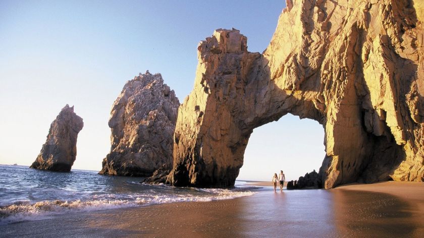 Um casal parado em uma praia perto de uma grande formação rochosa