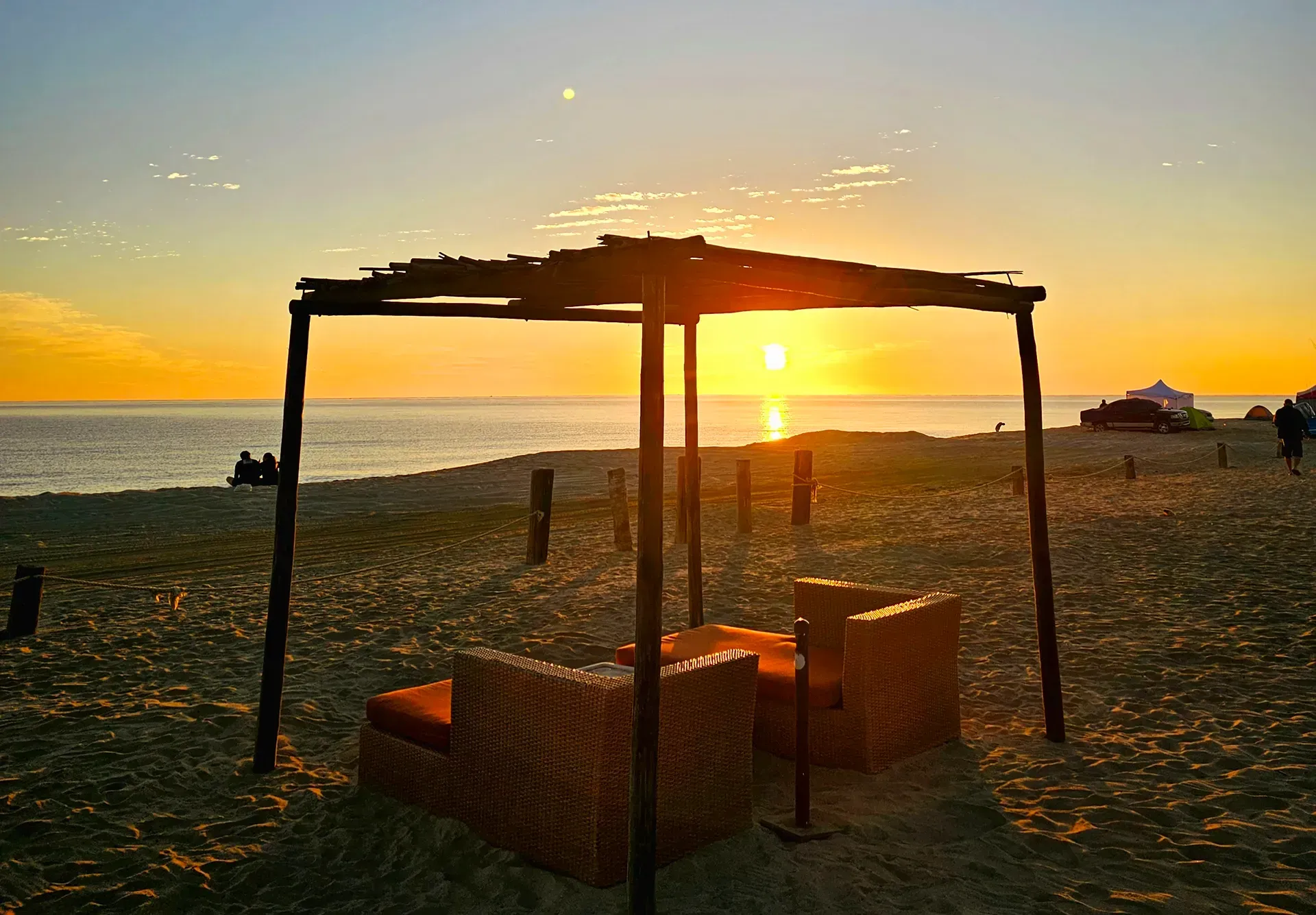 O sol está se pondo sobre o oceano e há um mirante na praia.