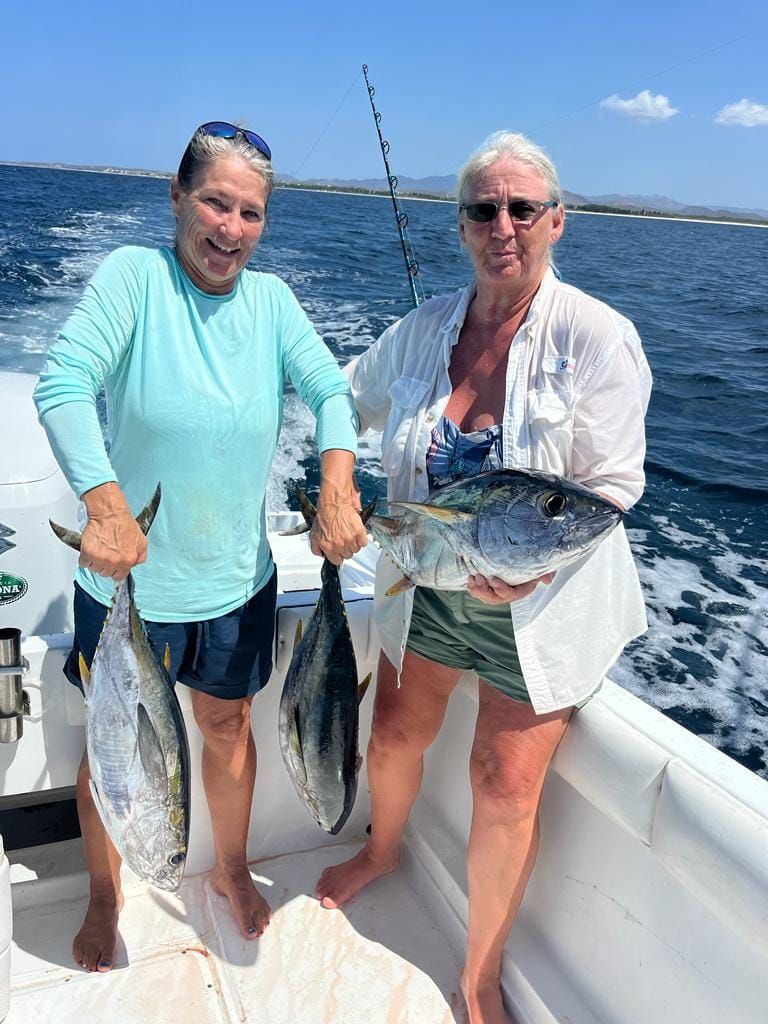 Dos mujeres están de pie en un barco sosteniendo peces.