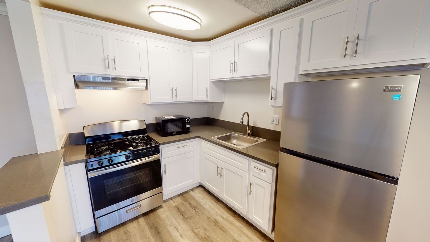 L-shaped kitchen with white cabinets, stainless steel appliances, and gray countertops.