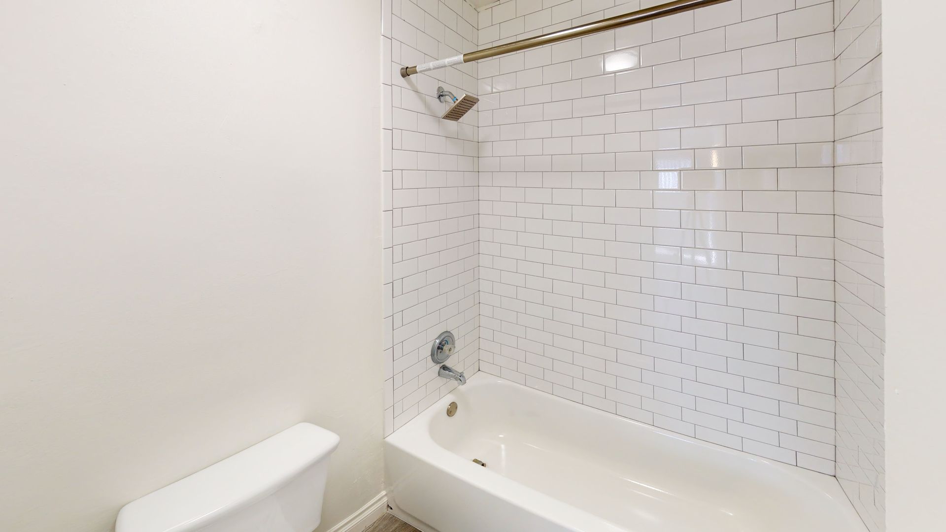 Bathroom with white tile shower, tub, toilet, and light-colored walls.