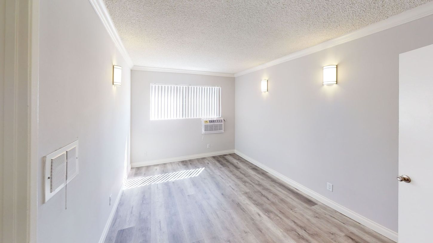 Empty room with light gray walls, wood-look floor, window with blinds, and two sconces.