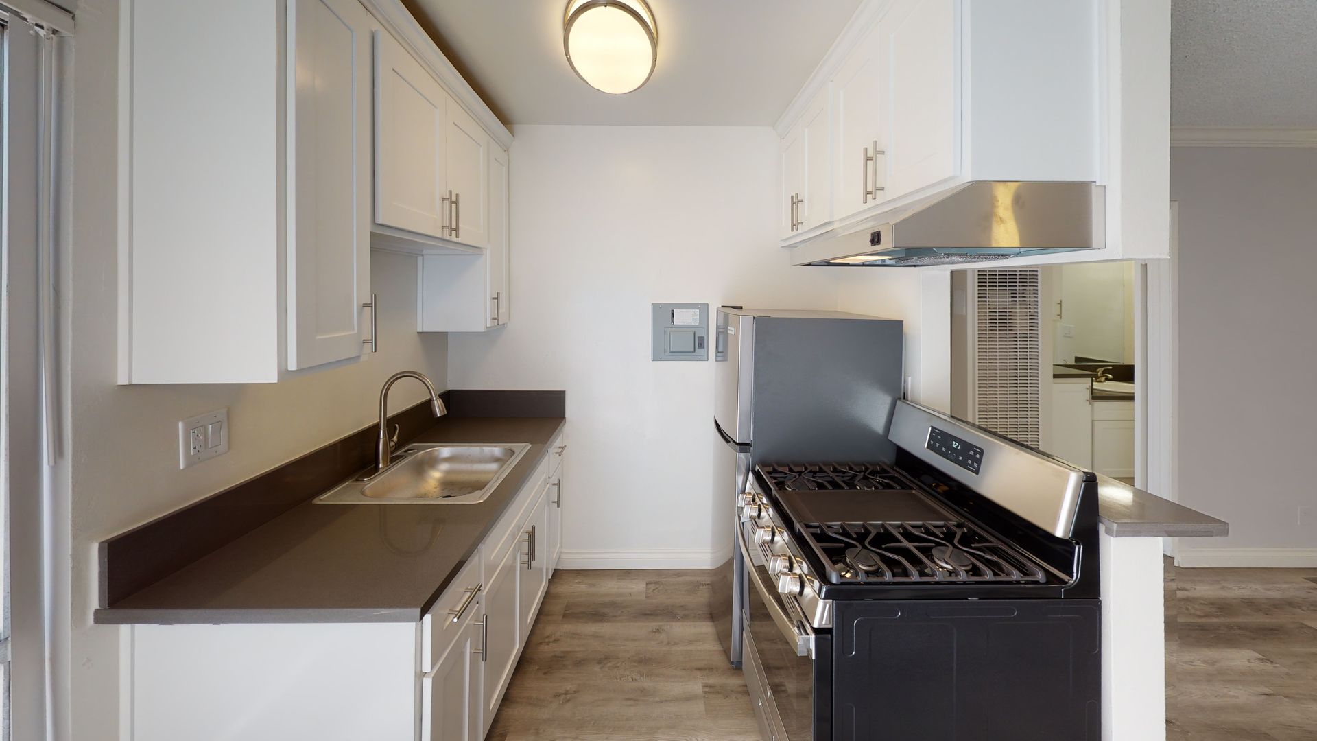 A galley kitchen with white cabinets, dark countertops, and stainless steel appliances.