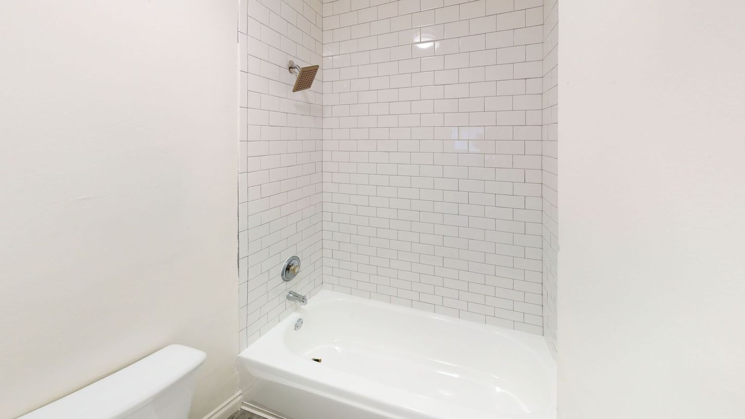 White bathroom with a tub, tiled shower walls, and a toilet.