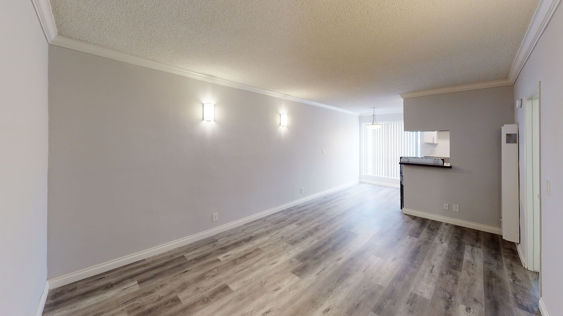Empty apartment interior with gray walls, wood flooring, and a view into the kitchen.