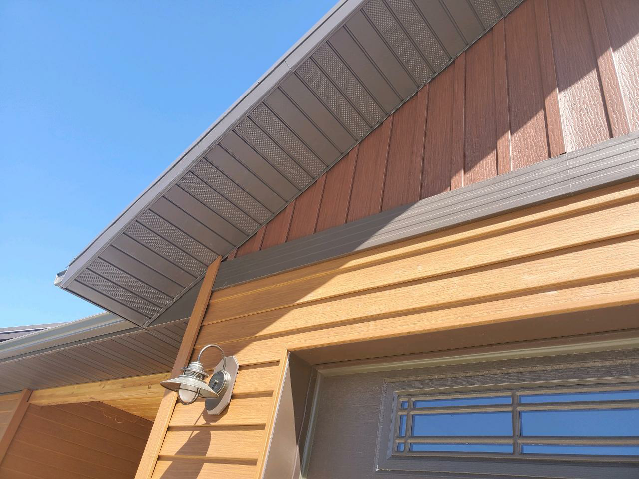 Brown and gray siding and soffit on a building, with a garage door and blue sky background.