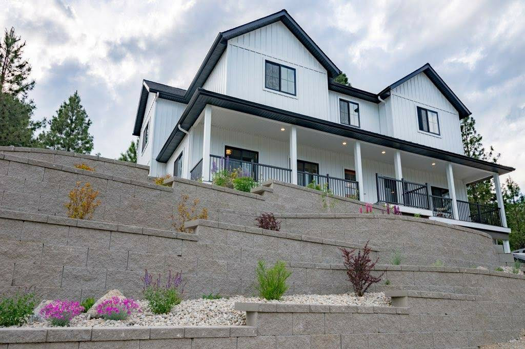 White farmhouse with black trim, built into a hillside with tiered retaining walls and landscaping.