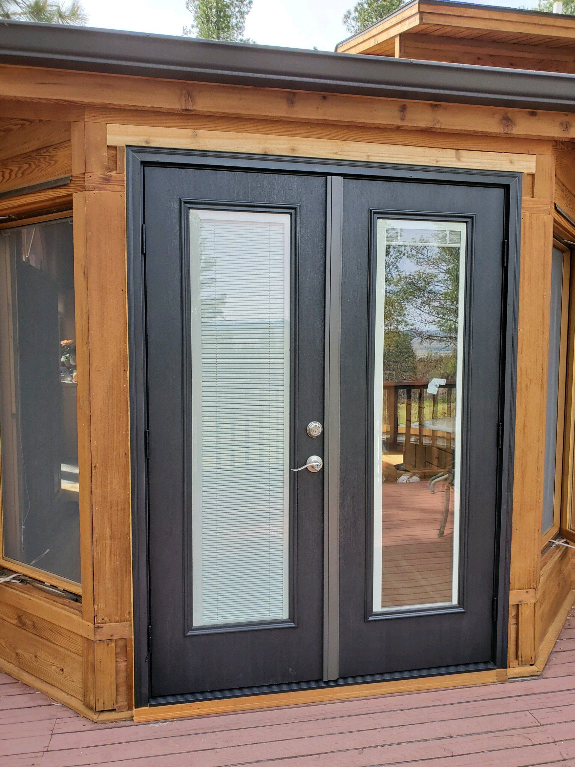 Black double doors with glass panels set in a wooden frame on a deck.