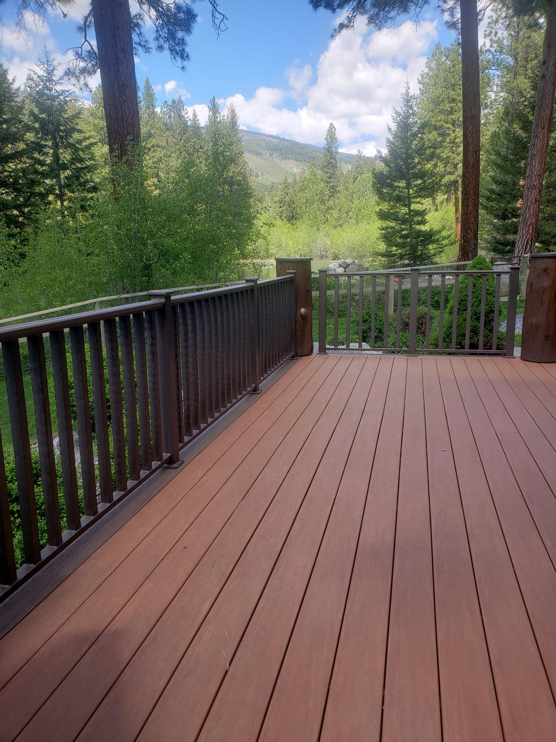 Wooden deck with a railing overlooking a forest and mountain landscape on a sunny day.