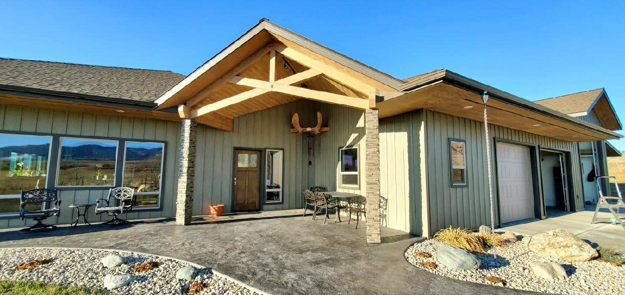 Exterior view of a house with a porch. The house has a wooden beam, stone columns and a concrete patio.