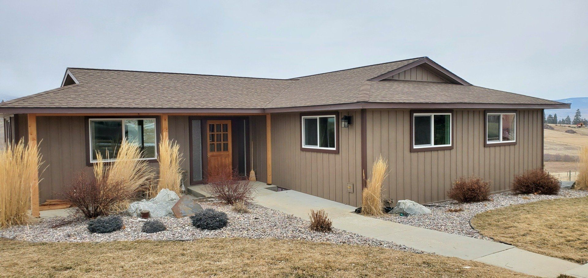 Brown house with a concrete walkway and landscaping. Cloudy sky.