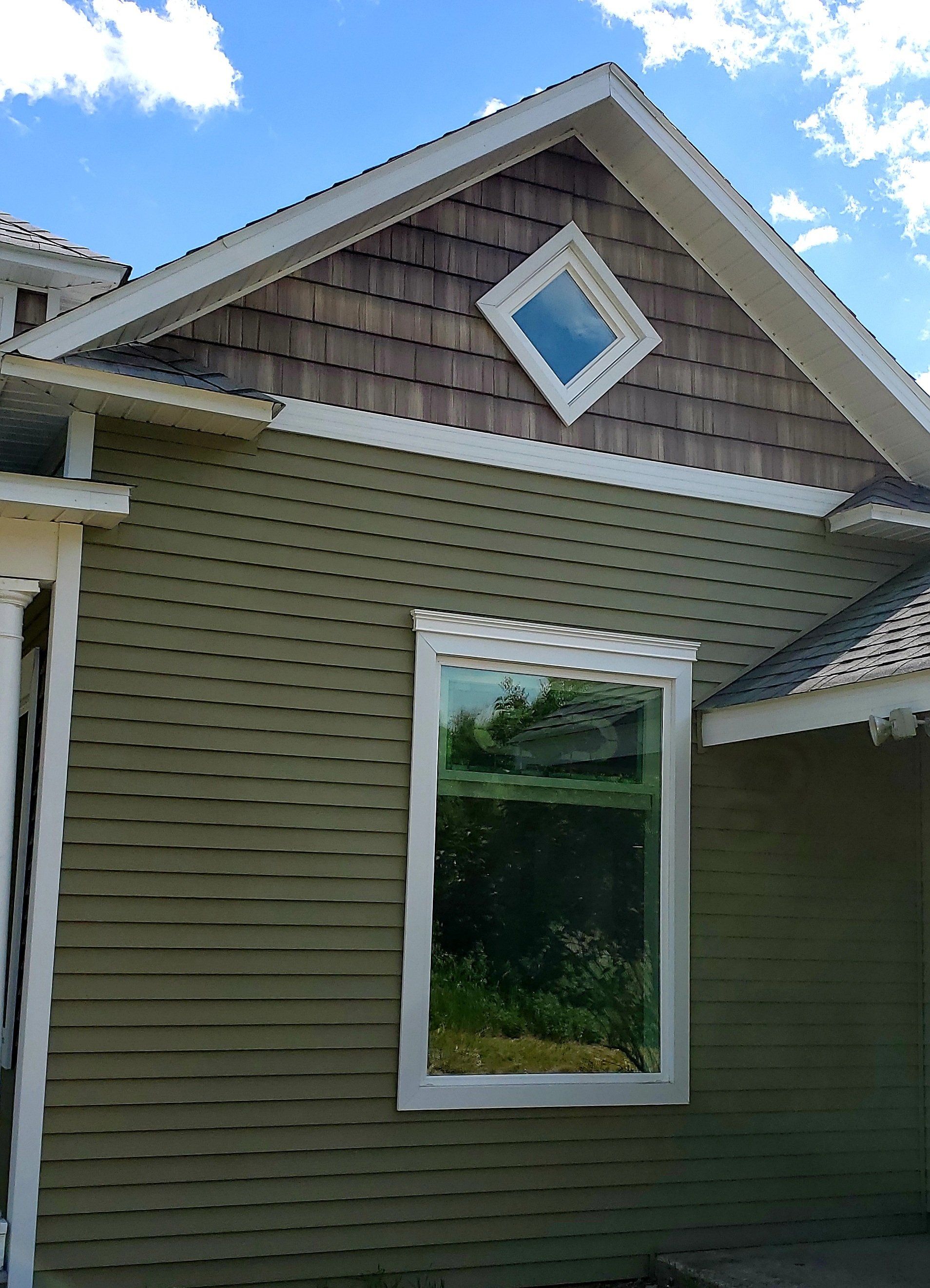 Green house exterior with diamond-shaped window, shingle siding, and a large rectangular window.
