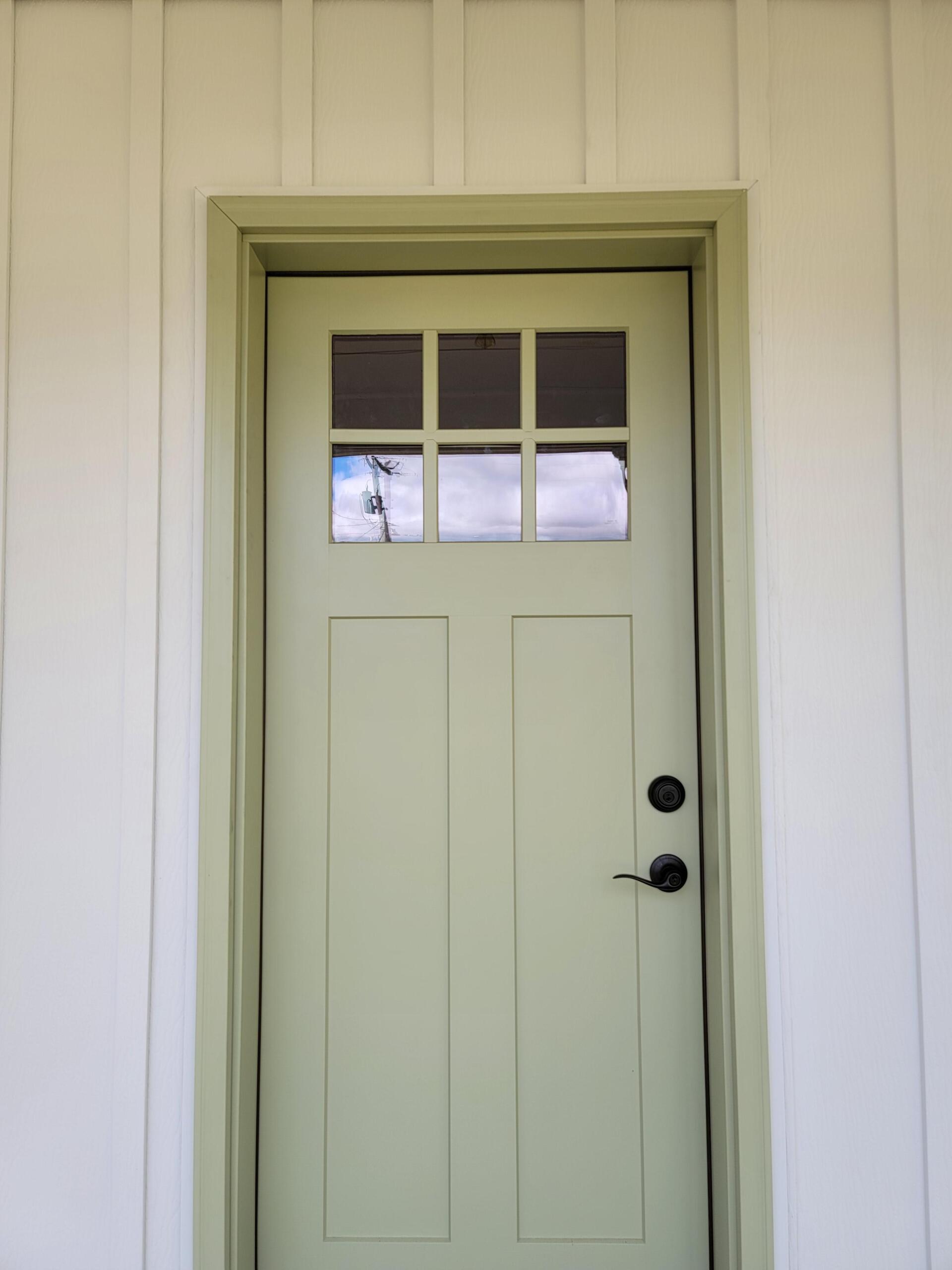Green door with glass panes, black hardware, and light green trim set in white siding.